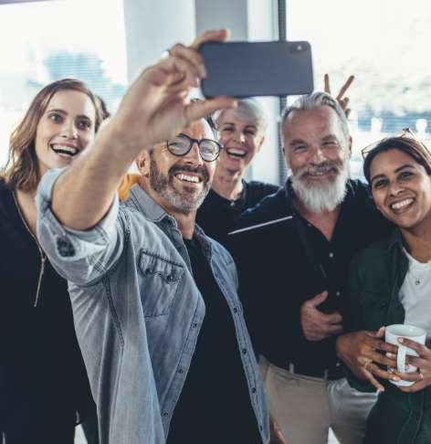 A group of happy company employees of various ages taking a group selfie A group of happy company employees of various ages taking a group selfie